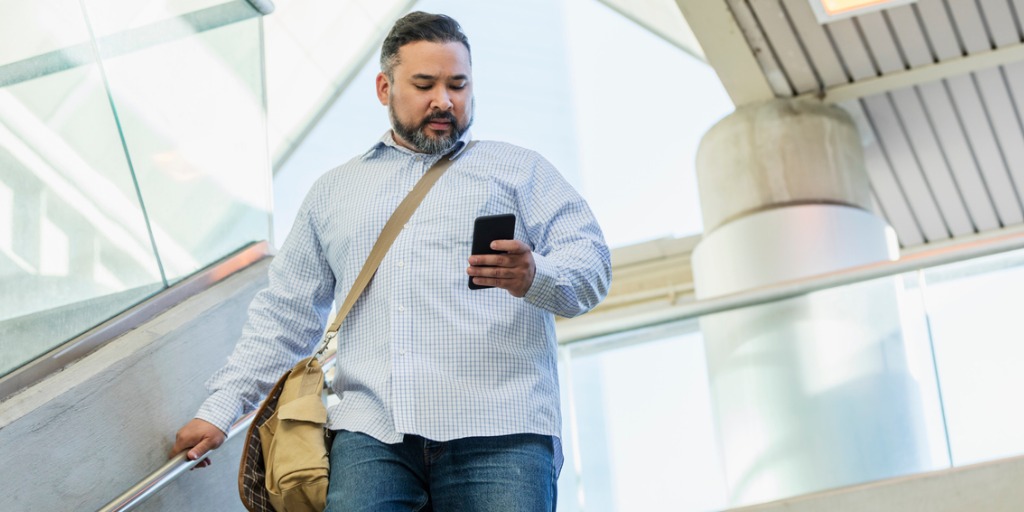 A man in his 30s wearing a button down shirt, walking down stairs outside a building, looking down at his mobile phone. A man in his 30s wearing a button down shirt, walking down stairs outside a building, looking down at his mobile phone.