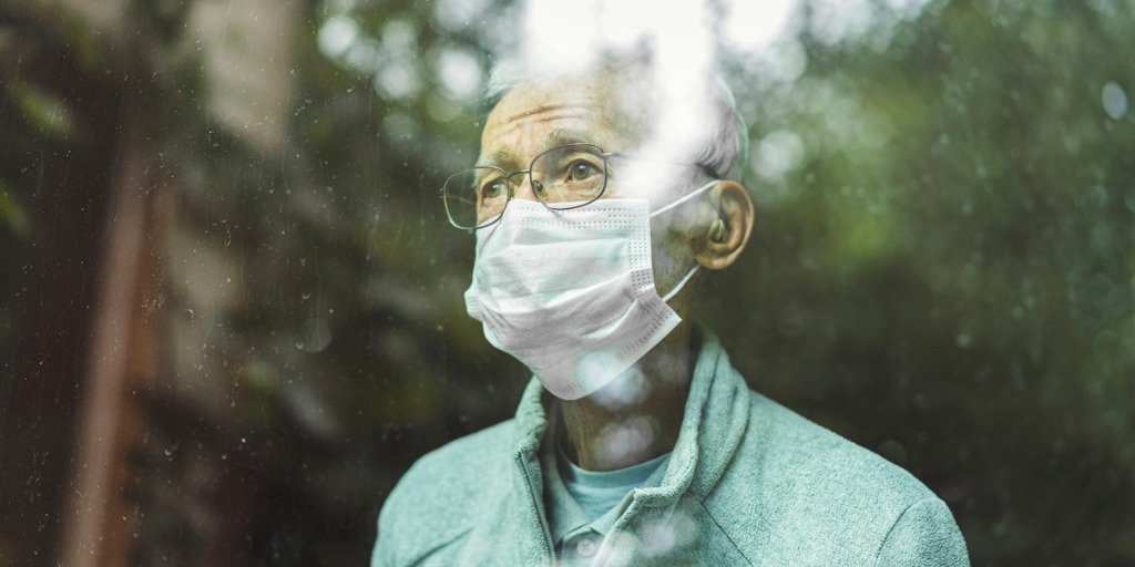 Senior man wearing mask looking through window.