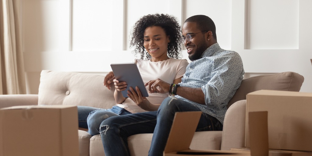 Couple sits on couch near boxes using tablet computer