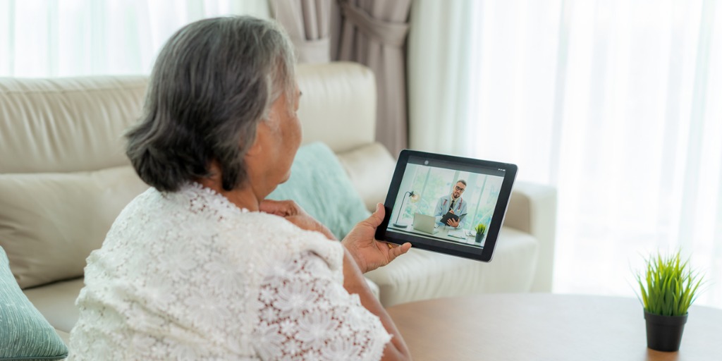 Back view of a woman making a video call with her doctor on a digital tablet.