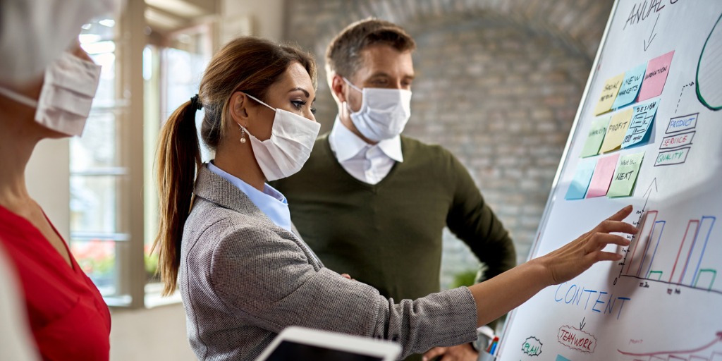 Businesswoman and her coworkers wearing protective face masks while making new business strategy on whiteboard during coronavirus epidemic. Businesswoman and her coworkers wearing protective face masks while making new business strategy on whiteboard during coronavirus epidemic.