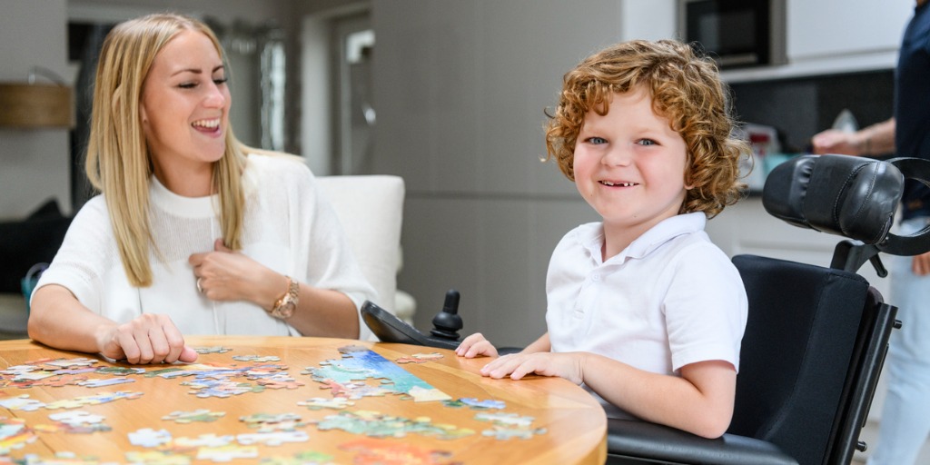 Cheerful boy in wheelchair doing jigsaw with his mother.