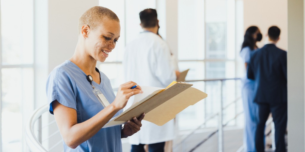 Nurse stands near the walkway railing as she reviews patient records.