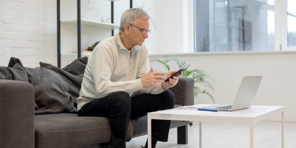 Busy older male working with smartphone and laptop while staying in living room Busy older male working with smartphone and laptop while staying in living room