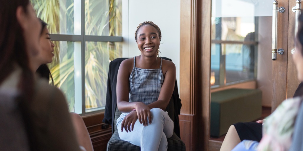 A young woman smiles while sharing her emotions and experiences with support group members.