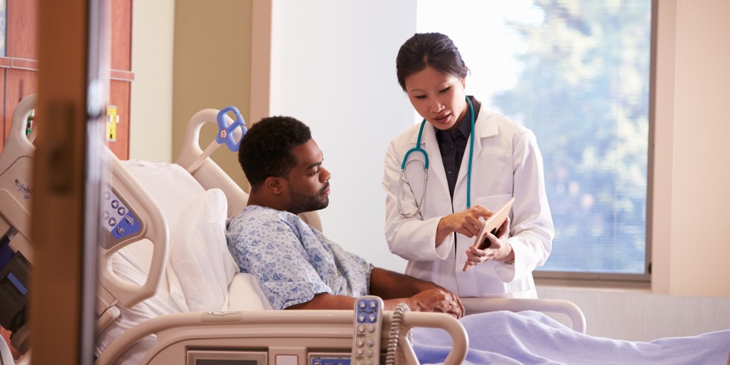 Hospital doctor with a digital tablet talks to a male patient.