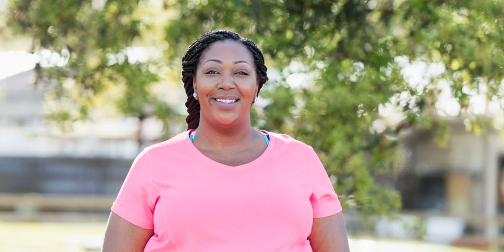 An adult woman with braided hair, wearing a pink t-shirt. She is smiling and looking at the camera.