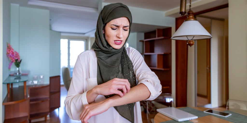 Woman at home itching her left arm.