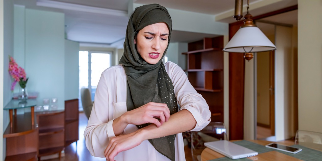 Woman at home itching her left arm. Woman at home itching her left arm.