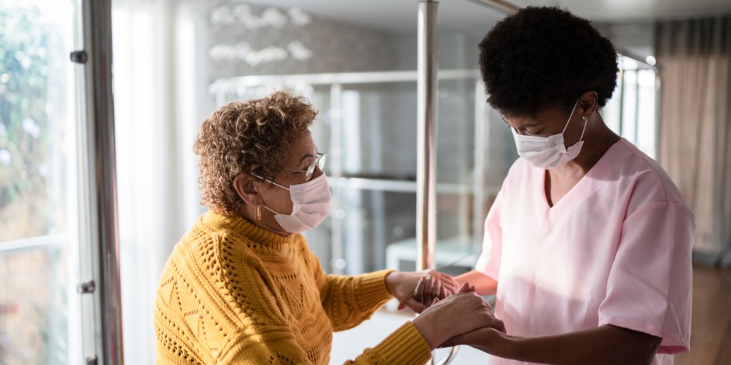 Nurse supporting senior patient walking or moving up the stairs at home