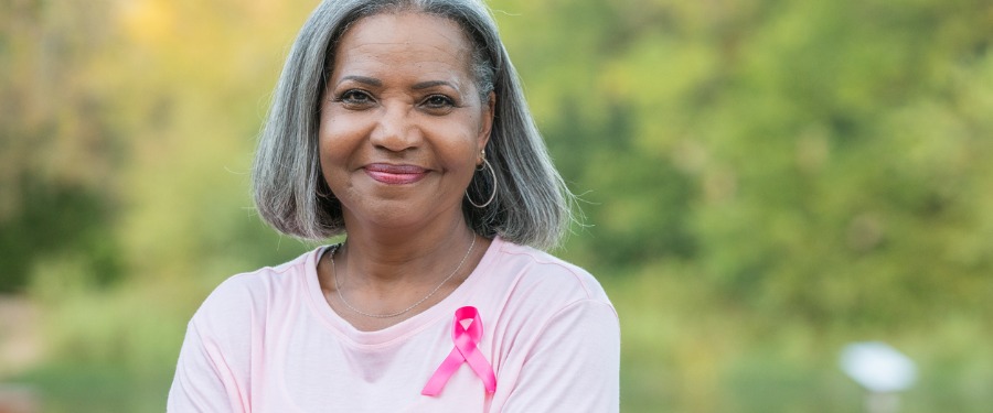 Black woman smiling with breast cancer ribbon pinned to her shirt