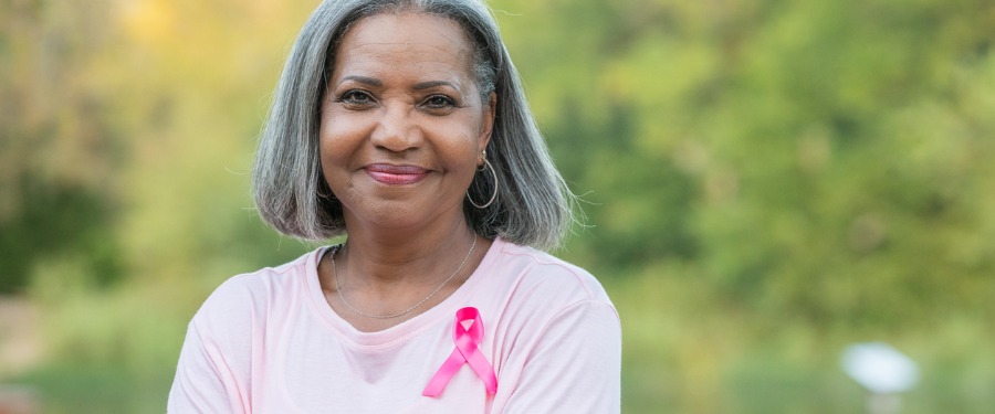 Black woman smiling with breast cancer ribbon pinned to her shirt Black woman smiling with breast cancer ribbon pinned to her shirt