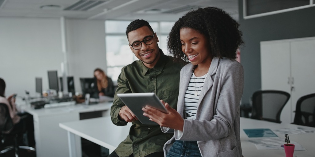 Young businesspeople sitting on desk using digital tablet while colleague in background at office