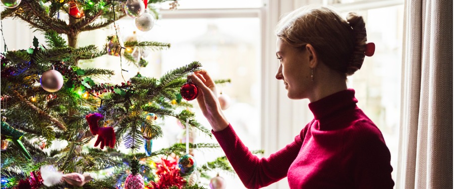 woman in red sweater hanging an ornament on a tree