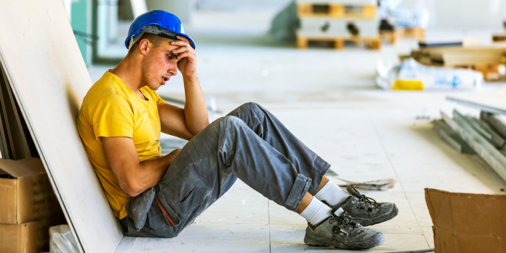 Male construction worker sitting down with pain in his abdominal region. Male construction worker sitting down with pain in his abdominal region.