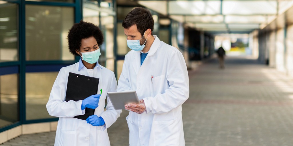 Two doctors looking at medical results on digital tablet in front of a hospital building.