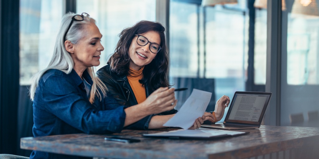 Two women analyzing documents while sitting at a table in the office.