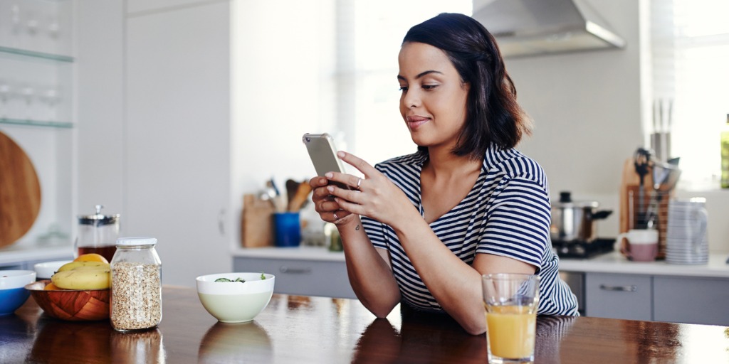 Woman using smart phone at kitchen table