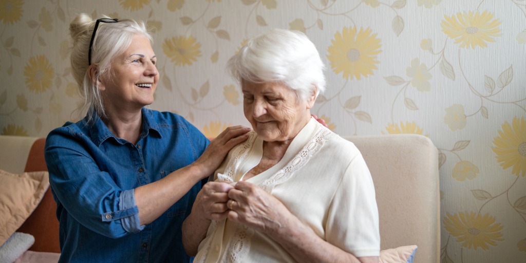 Woman helping senior woman dress in her bedroom