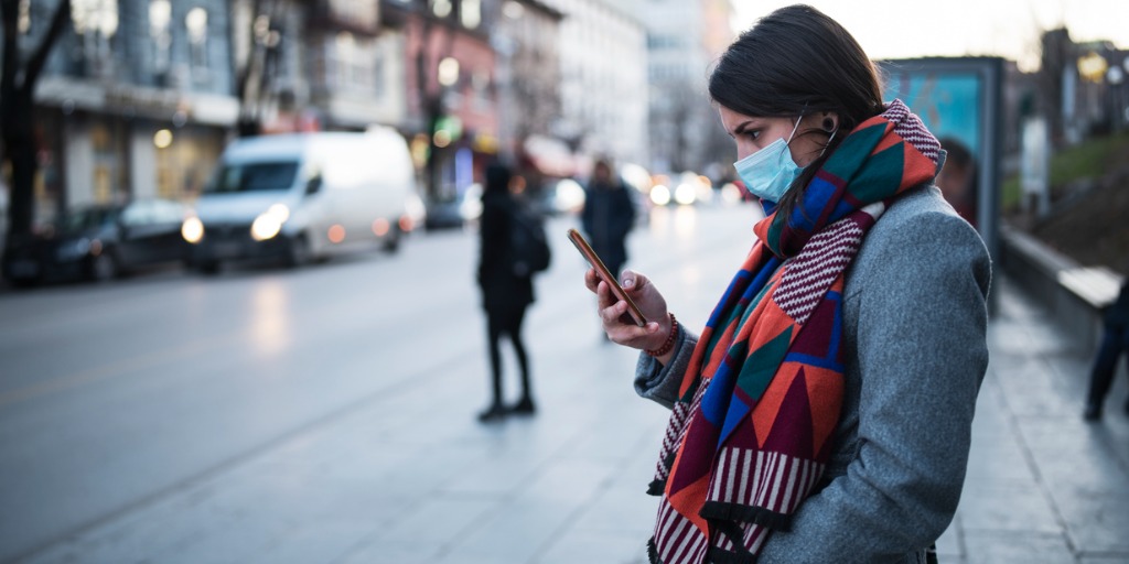 Woman with mask using cell phone on street.