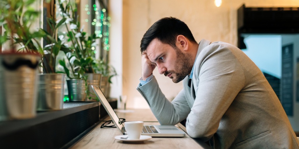 Worried man looking at laptop screen while sitting in an office cafe. Worried man looking at laptop screen while sitting in an office cafe.