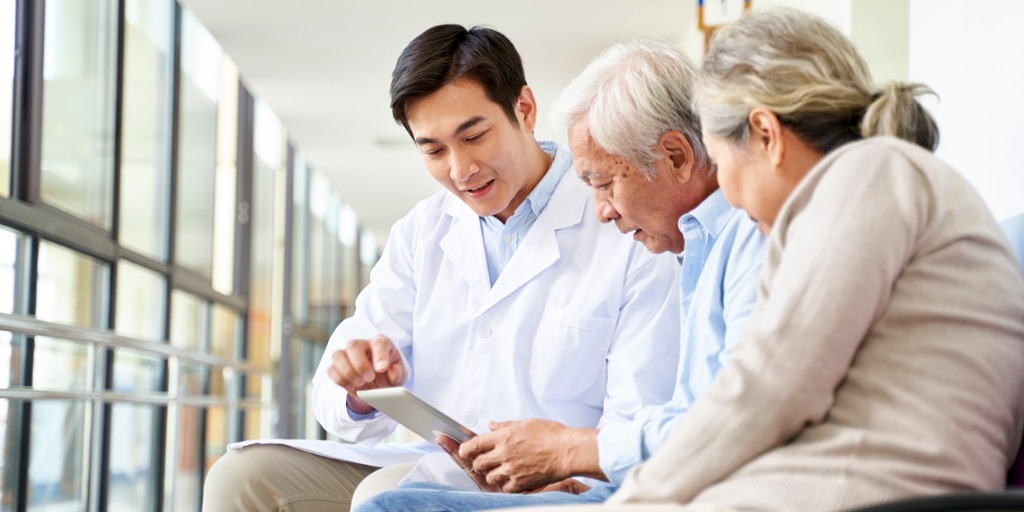 Young asian doctor discussing test result and diagnosis with senior couple patients using digital tablet in hospital hallway