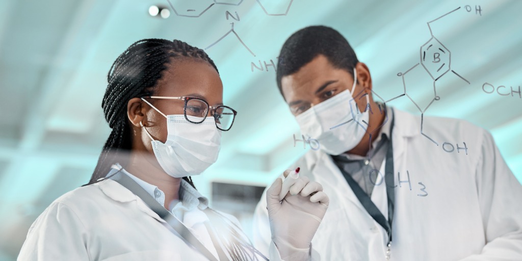 Two scientists drawing molecular structures on a glass wall in a lab