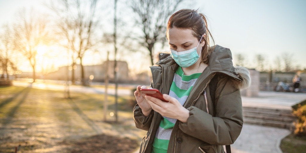 woman-with-mask-using-phone-in-the-city-park-picture-id1212893201